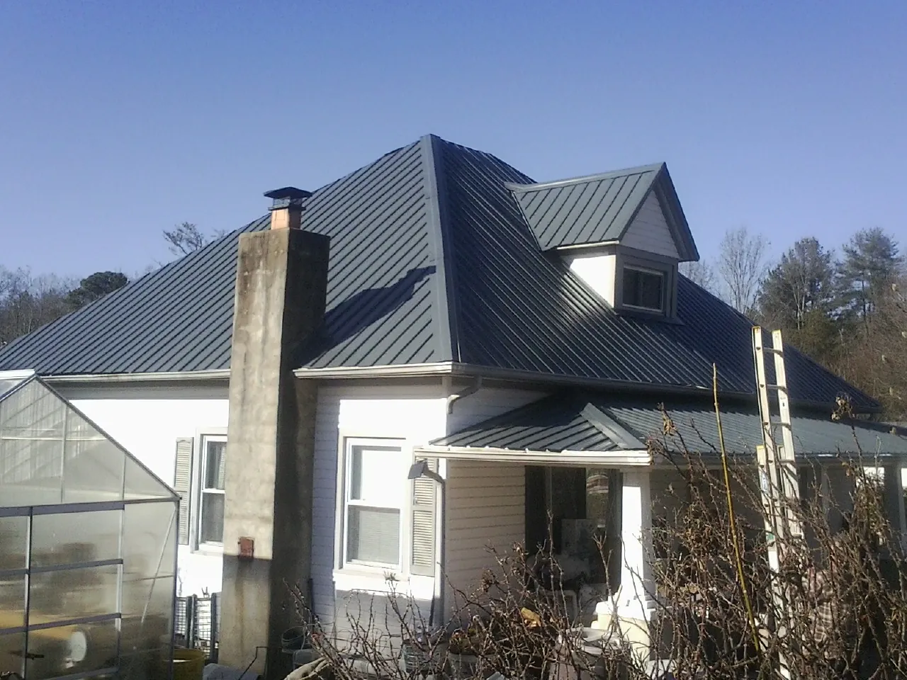 Dark blue standing seam metal roof on a white farmhouse with dormer — Slate & Tile Roof Repair by Roofing Brothers in Mill Creek